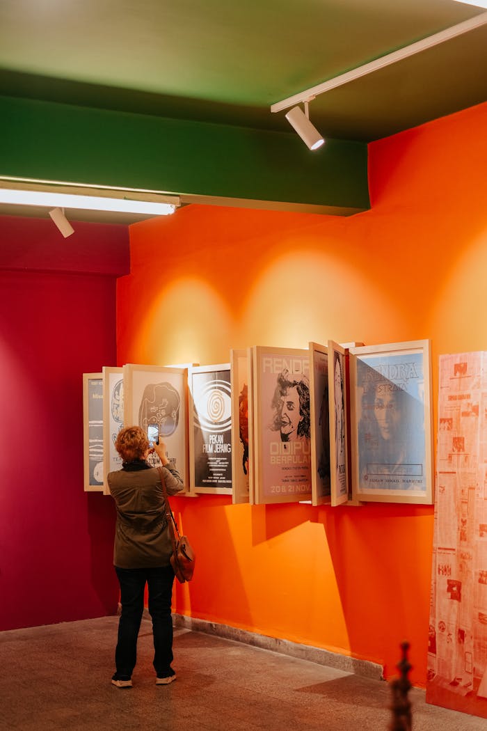 A person takes photos of modern posters in a bright, colorful art gallery exhibit.