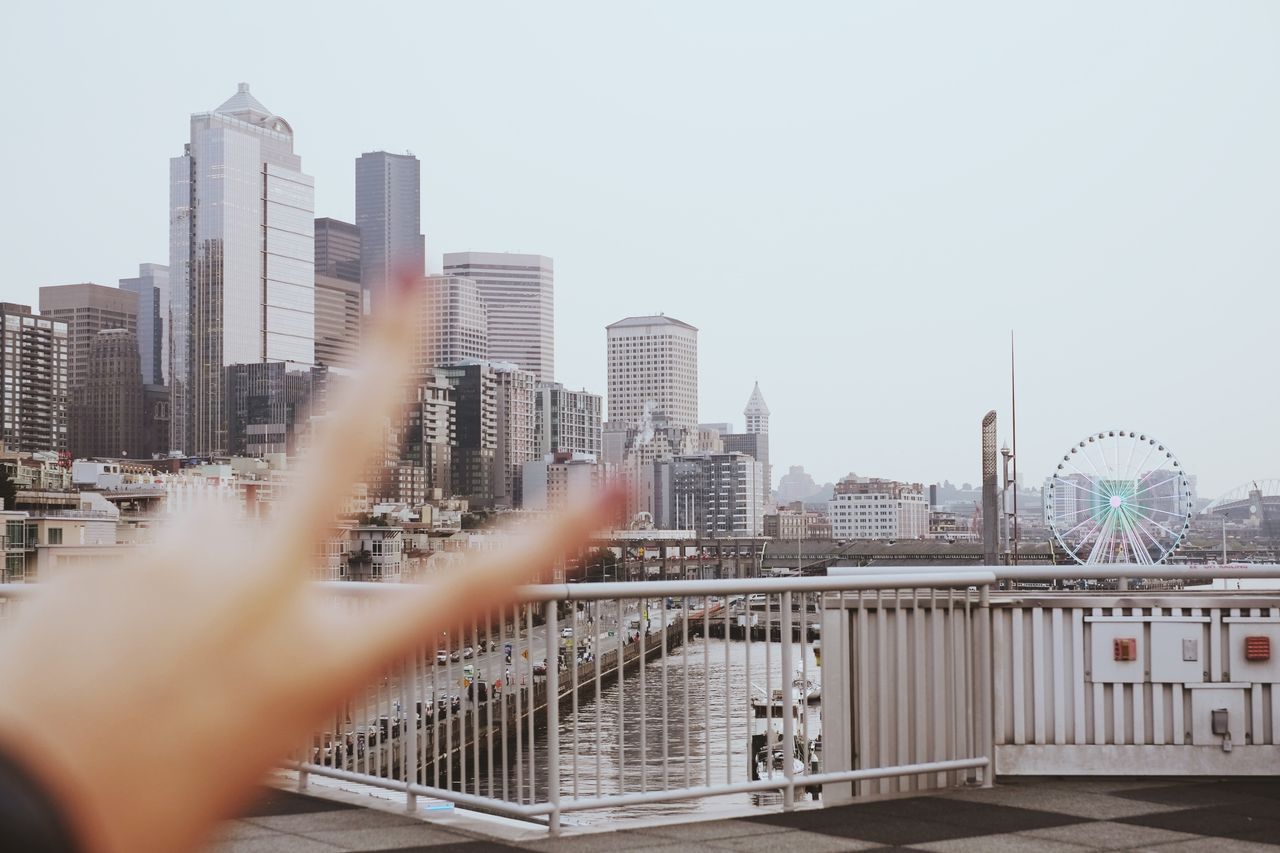A vibrant Seattle skyline view featuring modern architecture and a Ferris wheel with a peace sign gesture in the foreground.