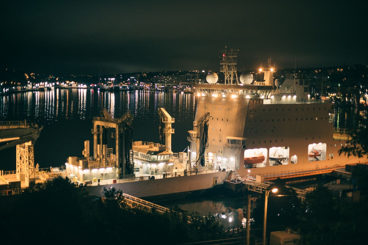A brightly lit cargo ship docked in a bustling harbor at night, showcasing city lights.