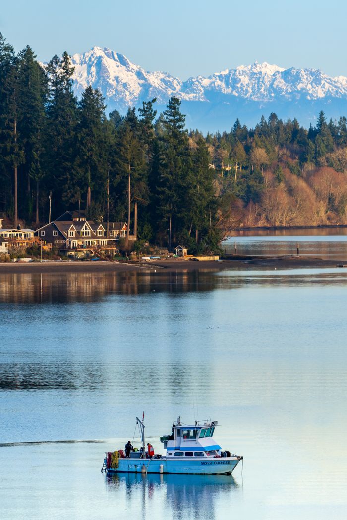 Tranquil morning scene with a fishing boat and snowcapped mountains in Washington, USA.
